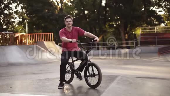 一个年轻人在他的自行车上有一个BMX自行车座椅与坡道溜冰公园的背景BMX骑手的肖像街道视频的预览图