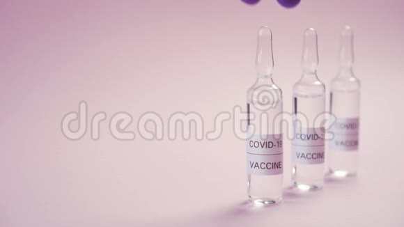 冠状病毒疫苗一只手戴着蓝色防护医疗手套在粉红色的表面上拿起安瓿视频的预览图