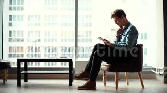 年轻的商务男士坐在椅子上使用现代小玩意视频的预览图