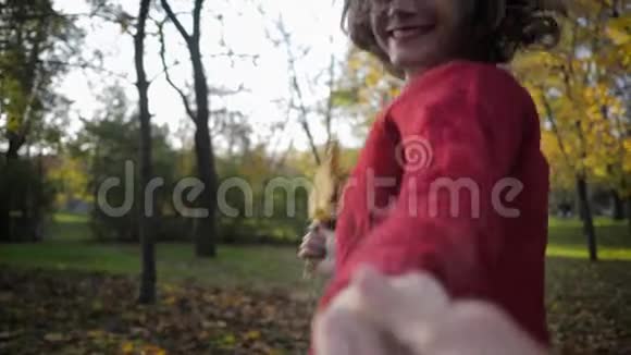 秋天戴着帽子的快乐微笑的女孩欢快地跑着微笑着手里拿着黄色的叶子在美丽的公园里视频的预览图