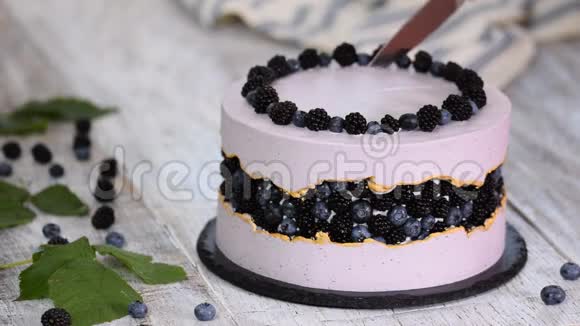 女人的手在切蛋糕紫色美丽的蛋糕装饰着浆果黑莓和蓝莓视频的预览图