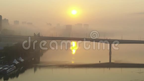 船在桥下漂浮城市和河流在黎明的雾中鸟瞰视频的预览图