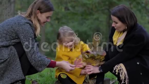 两个迷人的年轻女子和可爱的小女孩在公园的草坪上收集一束美丽的秋叶视频的预览图