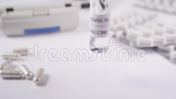 手把装有冠状病毒疫苗的安瓿放在带有医疗设备和胶囊的白色桌子上视频的预览图