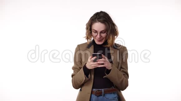 快乐的欧洲女人穿休闲服装的肖像棕色夹克和牛仔裤拿着智能手机和打字文本视频的预览图
