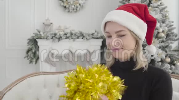 一位戴着红色帽子戴着黄色花环的漂亮白种人女子的特写镜头回顾着装饰好的新年树视频的预览图