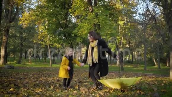 可爱的家庭年轻的妈妈带着开朗的小女儿带着雨伞在秋叶里玩得很开心散步视频的预览图