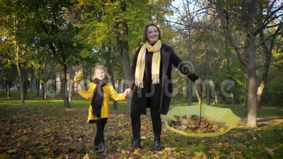 快乐的家庭可爱的妈妈和女儿在秋天的公园玩得开心从雨伞上洒下黄色的叶子视频的预览图