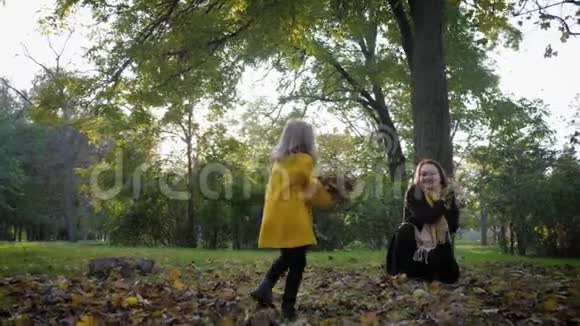 美丽的小女孩和她慈爱的妈妈在秋天公园玩落叶在家庭散步秋天的季节视频的预览图