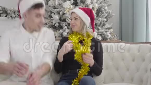 一幅迷人的白种女孩穿着圣诞服装坐在沙发上两个双胞胎兄弟来了年轻女子视频的预览图