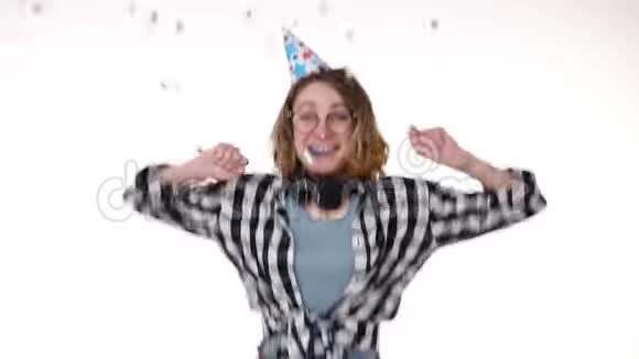 年轻女子穿着格子衬衫戴着耳机戴着生日礼物戴着五颜六色的帽子吹着烟斗跳舞视频的预览图