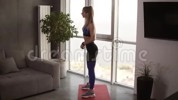 一个身材强壮肌肉发达的漂亮女孩正在明亮宽敞的客厅里做深蹲练习视频的预览图