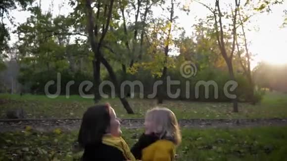 秋天的季节英俊的女儿坐在慈爱的母亲的怀里在秋天的公园里空地上玩投掷游戏视频的预览图