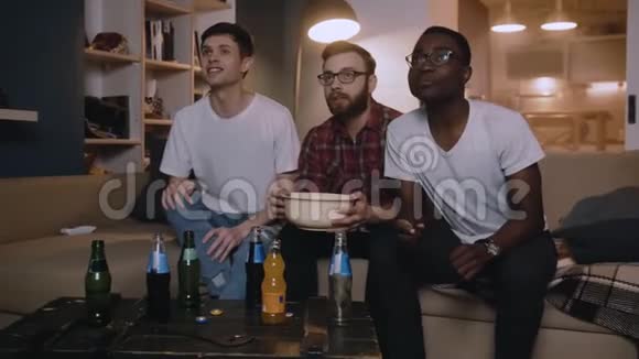 快乐的多民族青年男性体育迷们在家一起喊着看足球比赛带着零食慢动作视频的预览图
