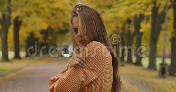 在秋天的公园里站在路上的棕色头发和愉快的微笑的冻白种人女孩的景色是个漂亮女人视频的预览图