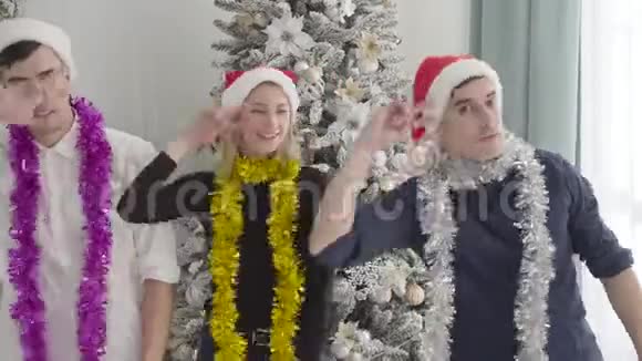 快乐的白人朋友在圣诞树前看镜头跳舞的肖像两个兄弟和两个兄弟视频的预览图