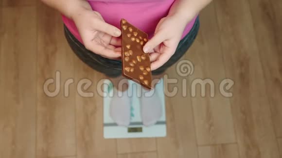 体重超重的女人站在秤上拿着巧克力视频的预览图