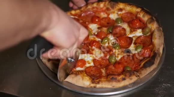 一个人用一个比萨饼切割器将一个意大利香肠比萨饼切成多片的慢动作特写视频的预览图