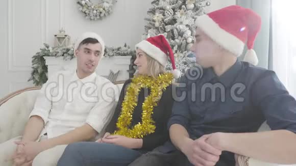 三个白种人的朋友坐在沙发上在阳光下装饰着圣诞树新朋友视频的预览图