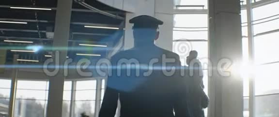 戴着帽子的老年飞行员穿过机场候机楼阳光照射视频的预览图