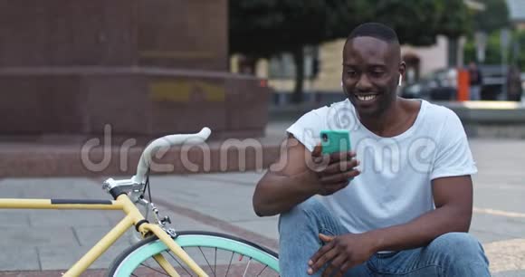 关闭兴奋的非洲裔美国人在耳机有视频通话和聊天通过他的智能手机男人笑视频的预览图