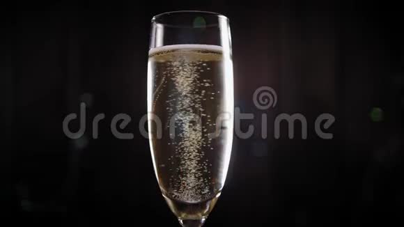 一杯香槟的特写镜头慢慢地在黑色背景上旋转背景上有灯光视频的预览图