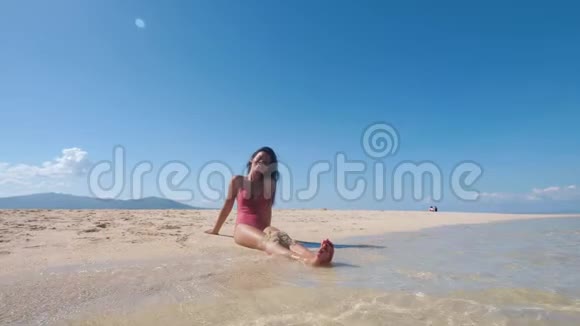 美丽的亚洲女孩穿着泳装日光浴坐在沙滩上微笑着视频的预览图