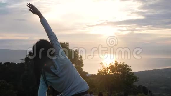 日出时在山上做热身运动的年轻女子的后景视频的预览图