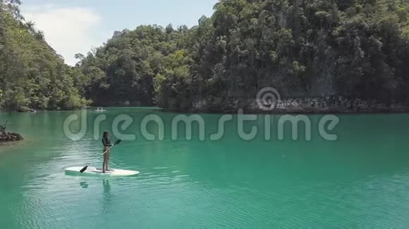 空中景色性感的女人站在美丽的绿松石泻湖上的桨板上视频的预览图