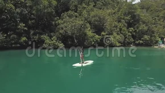 美丽的女人在亚洲宁静的泻湖中划桨无人驾驶的视野视频的预览图