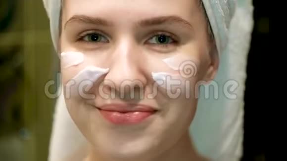 漂亮的年轻女人在浴室里把奶油涂在脸上概念为年轻妇女提供晚间和晨间面部护理视频的预览图