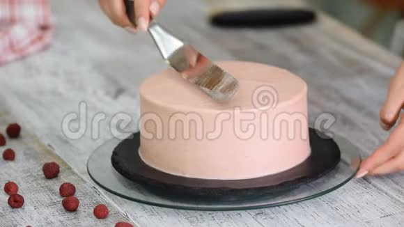 女糖果厨师用手用糕点刮刀和旋转蛋糕架装饰粉红色手工蛋糕视频的预览图