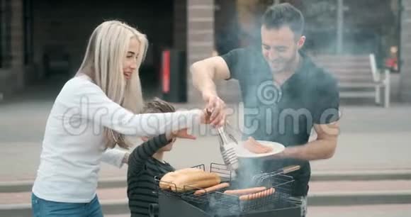 幸福的家庭在烤架上煮肉父亲和母亲带着儿子在烤架上煎香肠微笑着慢动作视频的预览图