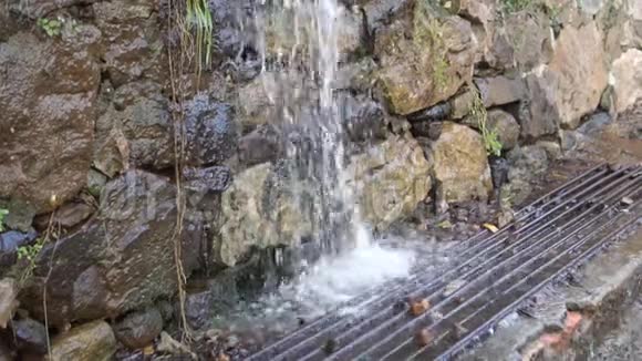 雨水和田落在一条小溪的下水道格栅上靠近一堵生石墙视频的预览图