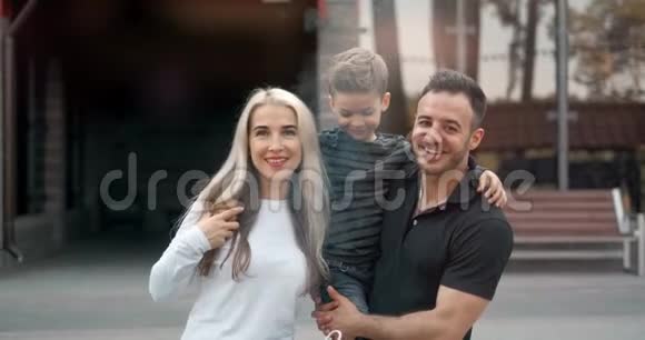 户外微笑幸福家庭的肖像带着孩子的父母正在看镜头视频的预览图