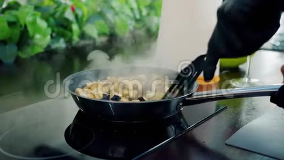 手拿手套在厨房的炊具上把切碎的蔬菜放在锅里煎视频的预览图