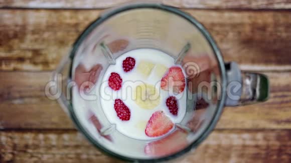 草莓香蕉和牛奶混合在桌子上的搅拌机里从上面看视频的预览图