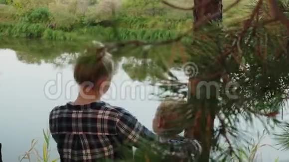 成年姐姐在松树林的河岸上拥抱弟弟快乐的少年女孩和男孩拥抱河视频的预览图