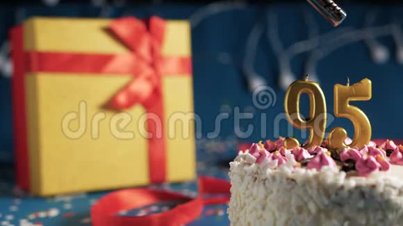 白色生日蛋糕数字95金蜡烛用打火机燃烧蓝色背景灯和礼品黄色盒子用红色系起来视频的预览图