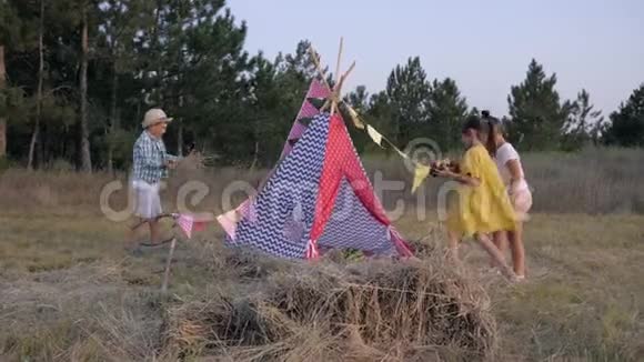 孩子们的游戏快乐的朋友在草地上装饰wigwam在森林的欢乐周末在森林里野餐视频的预览图