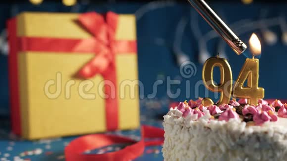 白色生日蛋糕编号94金色蜡烛由打火机燃烧蓝色背景灯和礼品黄色盒子与红色捆绑视频的预览图