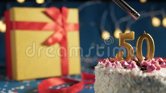 白色生日蛋糕数字50金蜡烛用打火机点燃蓝色背景灯和礼品黄色盒子系好视频的预览图