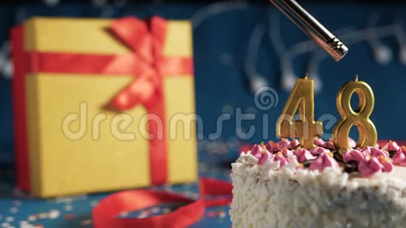 白色生日蛋糕编号48金烛由打火机点燃蓝色背景灯和礼品黄色盒子捆绑视频的预览图