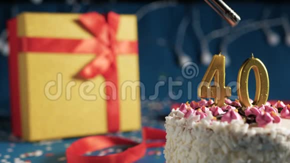 白色生日蛋糕数字40金蜡烛用打火机点燃蓝色背景灯和礼品黄色盒子系好视频的预览图