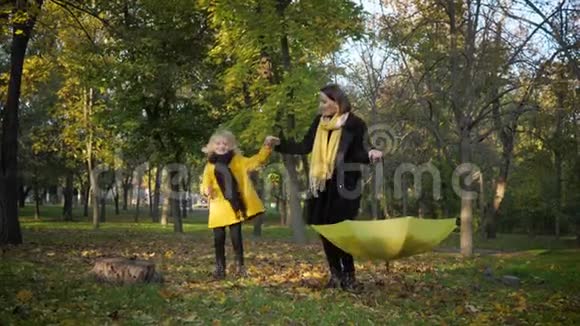 大家庭英俊的妈妈带着一个可爱的小孩子在秋天的树叶里打着伞在公园里散步视频的预览图