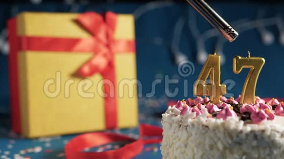 白色生日蛋糕编号47金色蜡烛用打火机燃烧蓝色背景灯和礼品黄色盒子捆绑视频的预览图