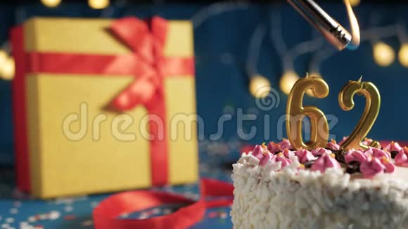 白色生日蛋糕数字62金蜡烛用打火机燃烧蓝色背景灯和礼品黄色盒子用红色系起来视频的预览图