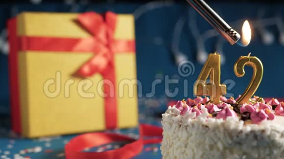 白色生日蛋糕42根金色蜡烛用打火机点燃蓝色背景还有黄色礼品盒视频的预览图