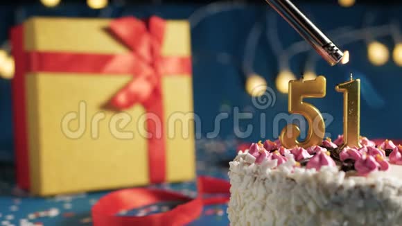 白色生日蛋糕编号51金色蜡烛由打火机燃烧蓝色背景灯和礼品黄色盒子捆绑视频的预览图
