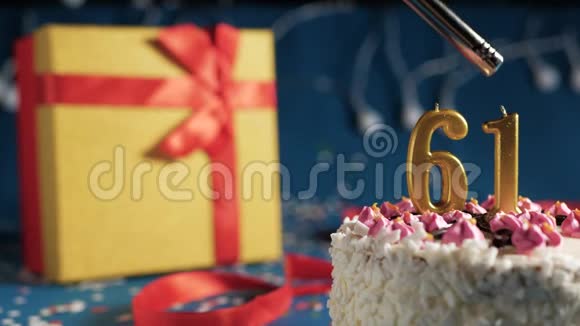 白色生日蛋糕数字61金蜡烛用打火机燃烧蓝色背景灯和礼品黄色盒子用红色系起来视频的预览图